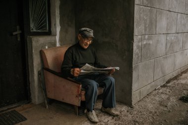 Gözlüklü, gri saçlı yaşlı bir adam gazete okuyor.