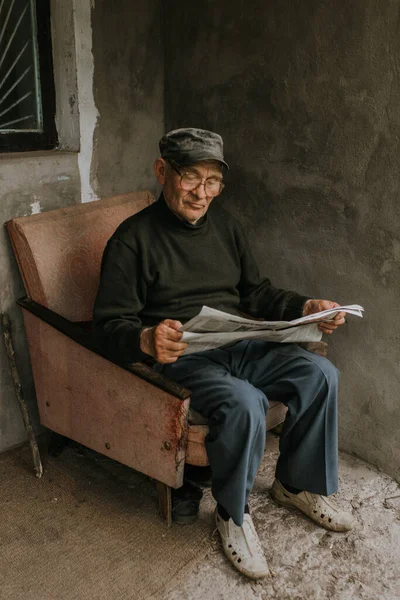 An old man in glasses with gray hair is reading a newspaper