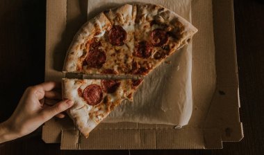 Peynirli ve salamlı bir pizza karton bir kutunun üzerinde duruyor.