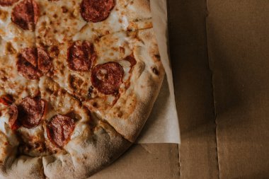 Peynirli ve salamlı bir pizza karton bir kutunun üzerinde duruyor.