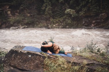 Sarışın bir kadın doğada yoga yapıyor.