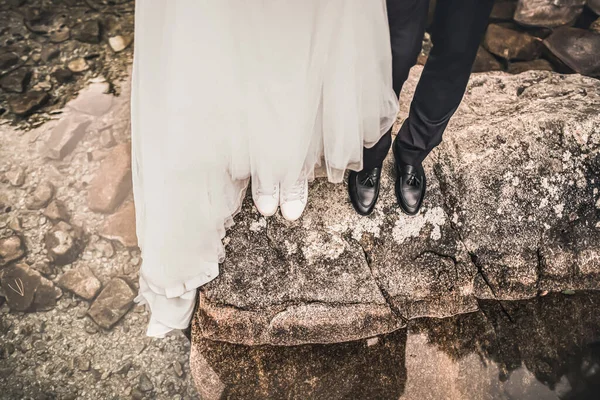 Las piernas de la novia y el novio de pie sobre piedra gris grande —  Fotos de Stock