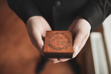 Bir adam oymalı kahverengi bir tahta kutu tutuyor..