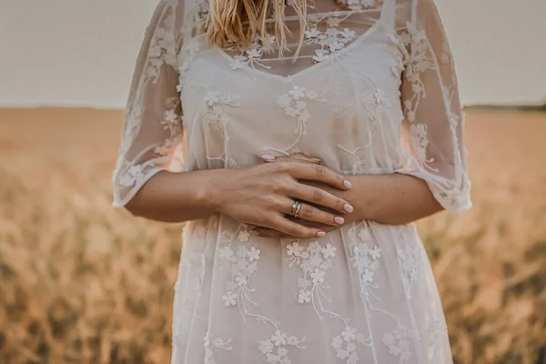 Una mujer en un vestido de novia blanco ajustado con un estampado floral se encuentra en medio del trigo —  Fotos de Stock