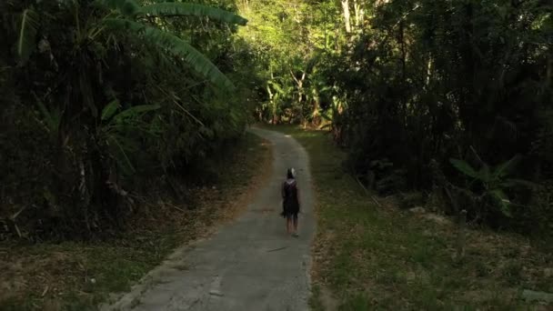 Mulher de moto capacete caminha ao longo da estrada no meio da selva escura verde — Vídeo de Stock