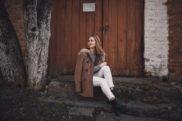 Женщина в коричневом пальто сидит на ступеньках — стоковое фото
