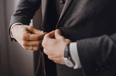 Siyah takım elbiseli bir adam ceketinin düğmesini ilikliyor.