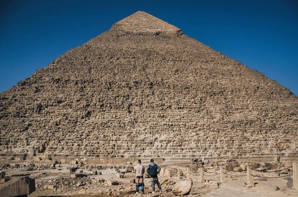 Due uomini in piedi davanti alla vecchia piramide con i pantaloni abbassati. — Foto Stock