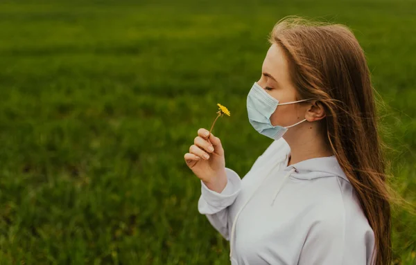 En flicka i respirator sniffar en gul maskros — Stockfoto