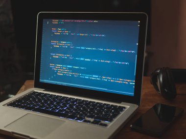 (Web geliştirme) dizüstü bilgisayar kodu. Programcı işyeri. Dizüstü bilgisayar, telefon ve kulaklık masada