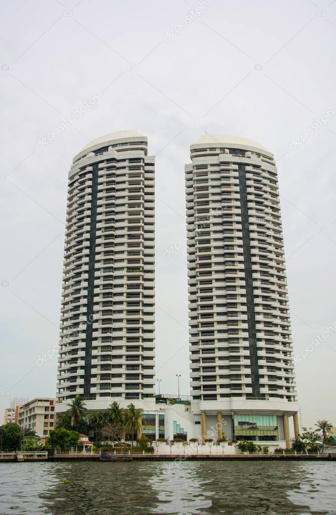 Two identical skyscrapers near canal in Bangkok under grey cloudy sky