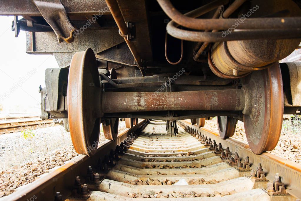 Underneath of an old freight train on the railroad tracks. Rusty wagon wheels on rusty gauge track