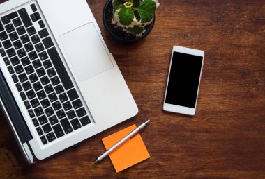 Laptop klavye etiket, kalem ve yeşil çiçek ile en iyi görünümünü ormanlık masada. cep telefonu ile boş siyah perde. Boşaltmak