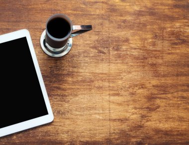 Tablet bilgisayar ve ahşap arka plan üzerinde kahve. En baştan görüntüleyin. Alanı, düz yatıyordu kopyalayın. Ahşap masa kahve ile boşaltmak tabletiyle parçası