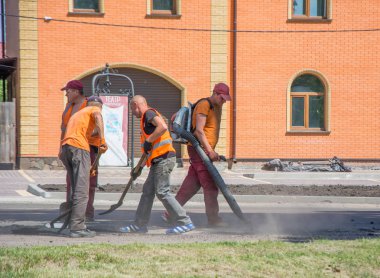 Nizhyn, Ukrayna - 25 Mayıs 2018: Asfalt kırıntı yol delik içine Yayilim için araçlarını kullanarak iş Tugayı. Asfalt kırıntı deliklere yaymak için yolun delikler topraktan dışarı üfleme bir işçi. Şehir içinde yol yenileme