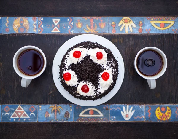 Flat lay. Cake with cherries, chocolate chips and two cups of tea on wooden table with egyptian pattern. Top view