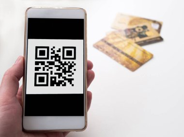Bar kod içeren telefon üstünde belgili tanımlık perde tutan el. Arka plan üzerinde üç kredi kartları. Nakitsiz satınalma