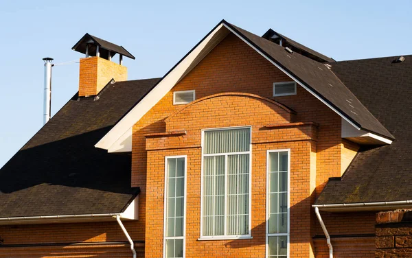 Modern cottage with multilevel roof, brick chimney, rain gutters and rectangular windows, suburban house facade