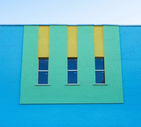 Three narrow vertical windows of green and yellow colors on the blue brick wall