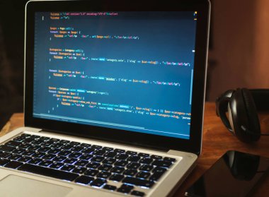 (Web geliştirme) dizüstü bilgisayar kodu. Kulaklık, telefon ve masanın üstünde laptop. Programcı çalışma alanı kavramı