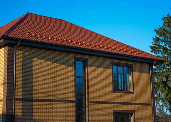 Two-storey house with tall vertical window on the stairwell, rain-gutter and show-guard on the metal tiled roof