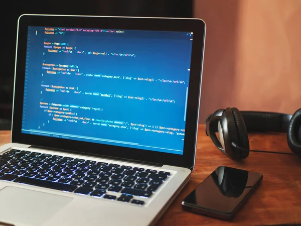 (Web geliştirme) dizüstü bilgisayarınızın ekranında bilgisayar kodu. Smartphone, kulaklık ve tablo, çalışma alanı kavramı üstünde laptop