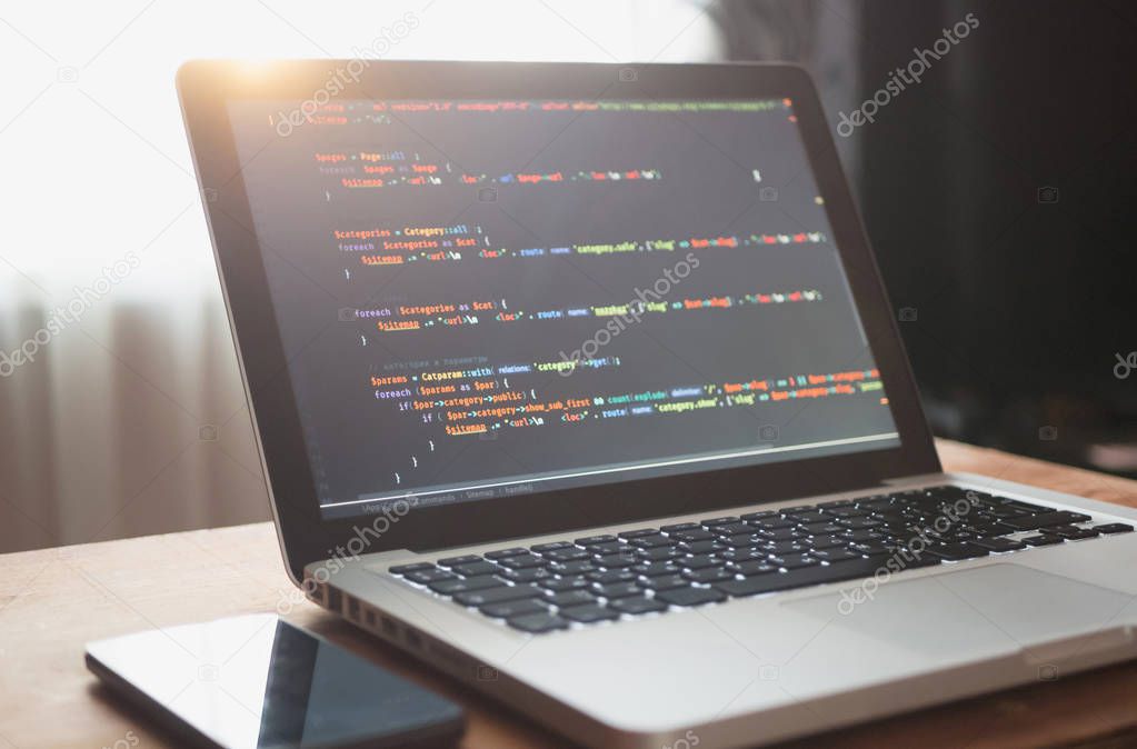 Computer code on laptop (web developing) and mobile smart phone in sunlight