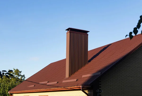 Chimney made of profiled sheeting on the roof with rain gutters and snow guards on the sunset