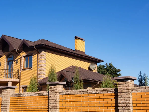 Big brick home with chimney, rain gutter and brick fence under clear blue sky, side view