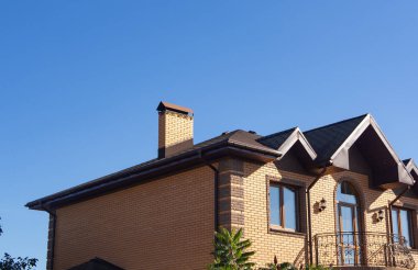 Açık mavi gökyüzü altında güzel dövme ile modern tuğla baca. Modern tuğla ev balkon, pencere eşiği ve yağmur olukları ile dış
