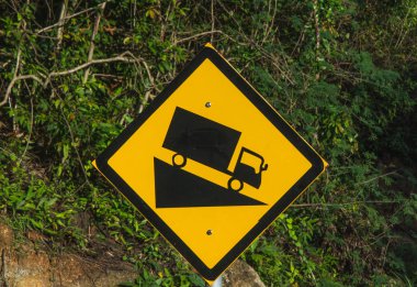 Steep road sign with a truck driving down the abrupt slope. Rainforest background. In black and yellow colors. clipart
