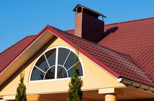 Ventana semicírculo y chimenea de ladrillo en el techo de azulejos de metal rojo, exterior de la casa — Foto de Stock