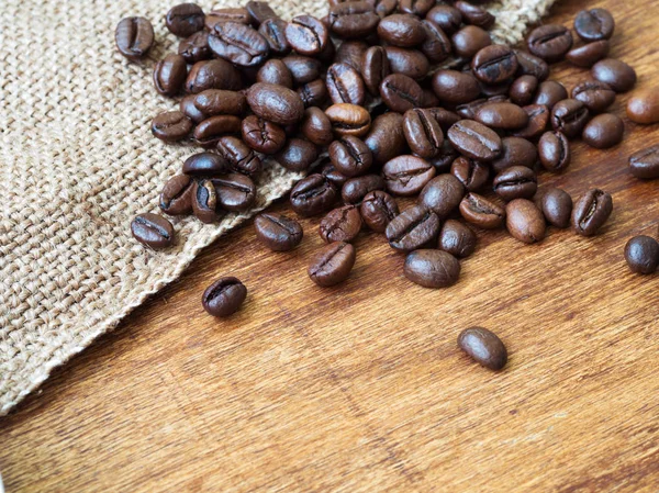 Primer plano de granos de café tostados sobre tela de saco, fondo de madera —  Fotos de Stock