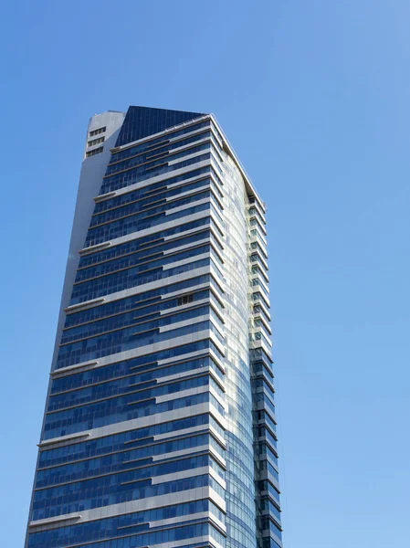 Сучасний хмарочос зі скляним фасадом і білими смугами на тлі блакитного неба, вертикальний — стокове фото