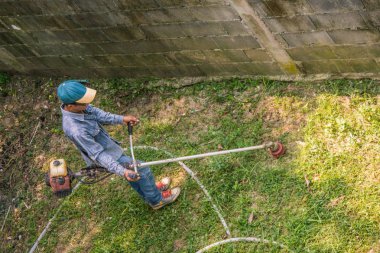 Asyalı adam benzinfırça kesici kullanarak çim kesme