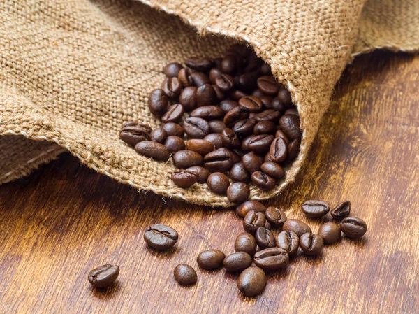 Macro de granos de café en saco sobre mesa de madera —  Fotos de Stock