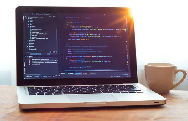 Dizüstü bilgisayarda Php kodu (web geliştirme) ve güneş ışığında beyaz kupa