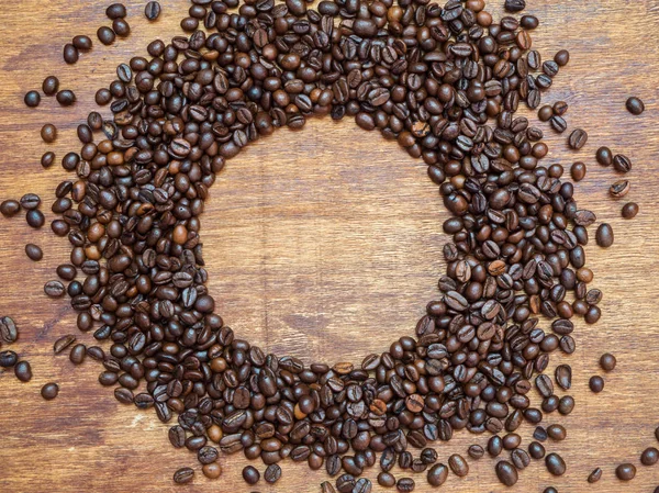 Circle frame made of coffee beans on wooden background. View from above. Coffee background