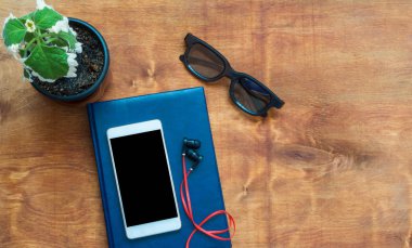 Kırmızı kulaklıklı akıllı telefon, mavi dizüstü bilgisayar ve siyah gözlüklü