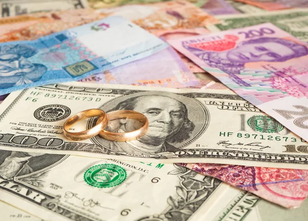 Golden wedding rings on different currencies. Marriage of convenienced — Stock Photo, Image