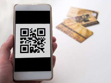 Ekranda qr kodu ile el tutan telefon. Arka planda kredi kartları. Nakitsiz satın alma