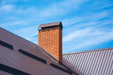 Berrak mavi gökyüzü altında çatıda dövme ve kar korumaları ile Modern tuğla baca