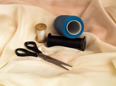 Bej kumaş üzerinde siyah makas ve iplikler, closeup,