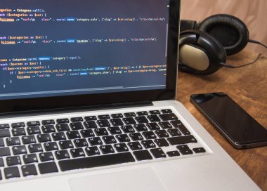 Programcı çalışma yerinde cep telefonu ve kulaklık ile dizüstü bilgisayar ekranında Php kodu