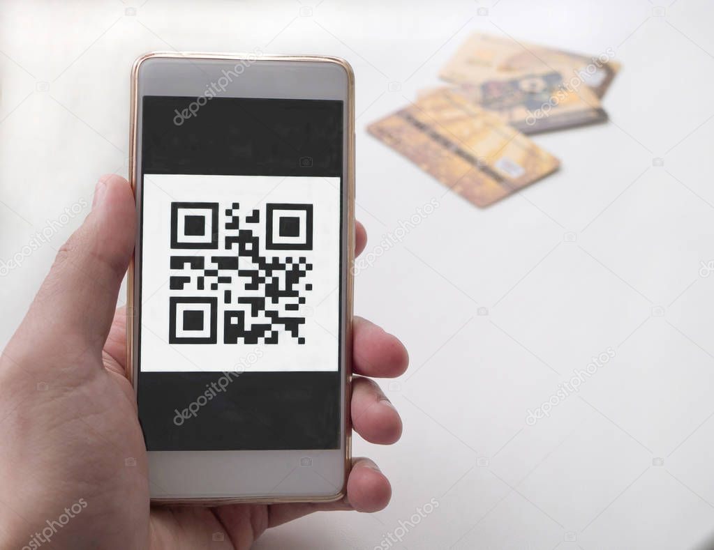 Hand holding smart phone with QR code. 3 bank cards on backgroun