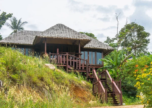 Wooden bungalow with stairs and thatched roof among palm trees under blue sky — Stock Photo, Image