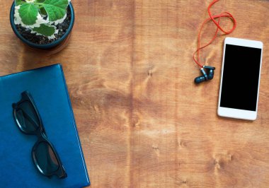 Ahşap masa üzerinde dizüstü bilgisayar, cep telefonu, kulaklık ve siyah gözlük