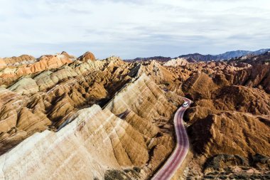 Üstten Görünüm gökkuşağı dağlar jeolojik park. Çizgili Zhangye Danxia ılık jeolojik Park Gansu Eyaleti, Çin. Turist otobüsleri güneşli bir günde bir vadide bir yolda resmini uçak.