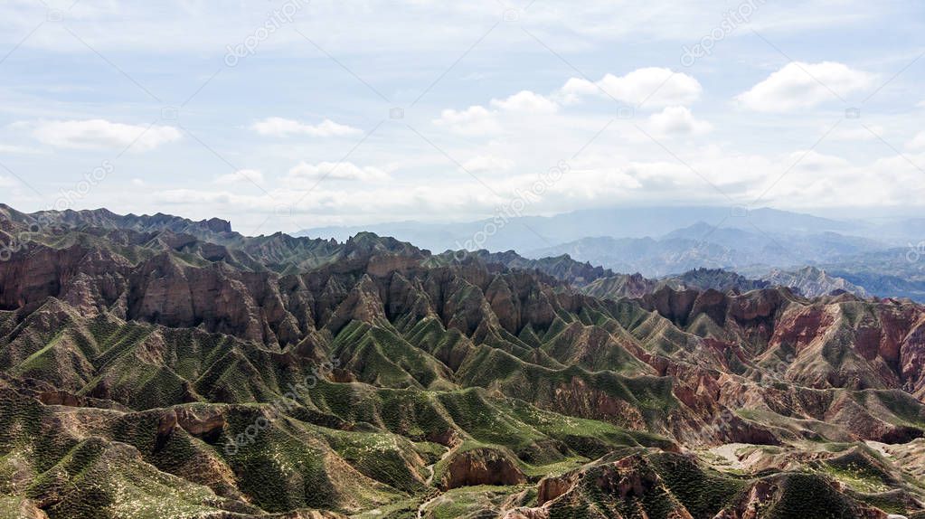 Aerial View of Binggou Danxia Canyon Landform in Zhangye, Sunan Region, Gansu Province, China. Sharp Pointy Peaks in the Geopark. Low Clouds and Blue Sky on a Sunny Day.