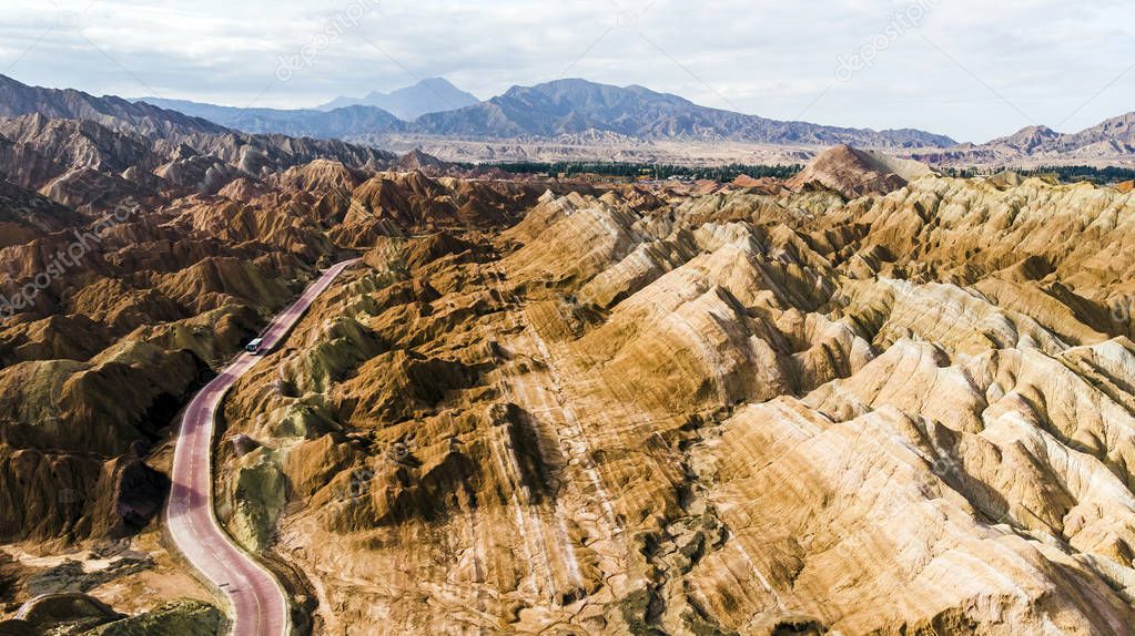 Top View of Rainbow Mountains Geological Park. Stripy Zhangye Danxia Landform Geological Park in Gansu Province, China. Drone Picture of Tourist Buses on a Road in a Valley on a Sunny Day.